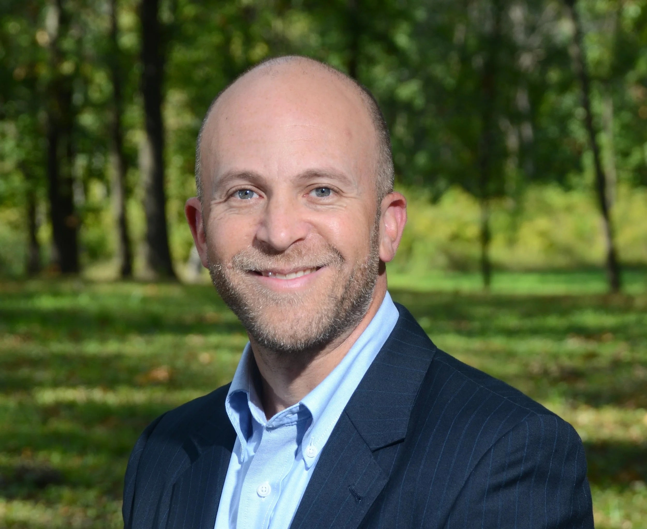 Man in a suit standing outdoors with trees in the background